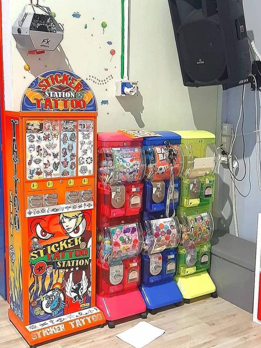 Distributore di sticker e tatuaggi arancione accanto a tre distributori di palline colorati